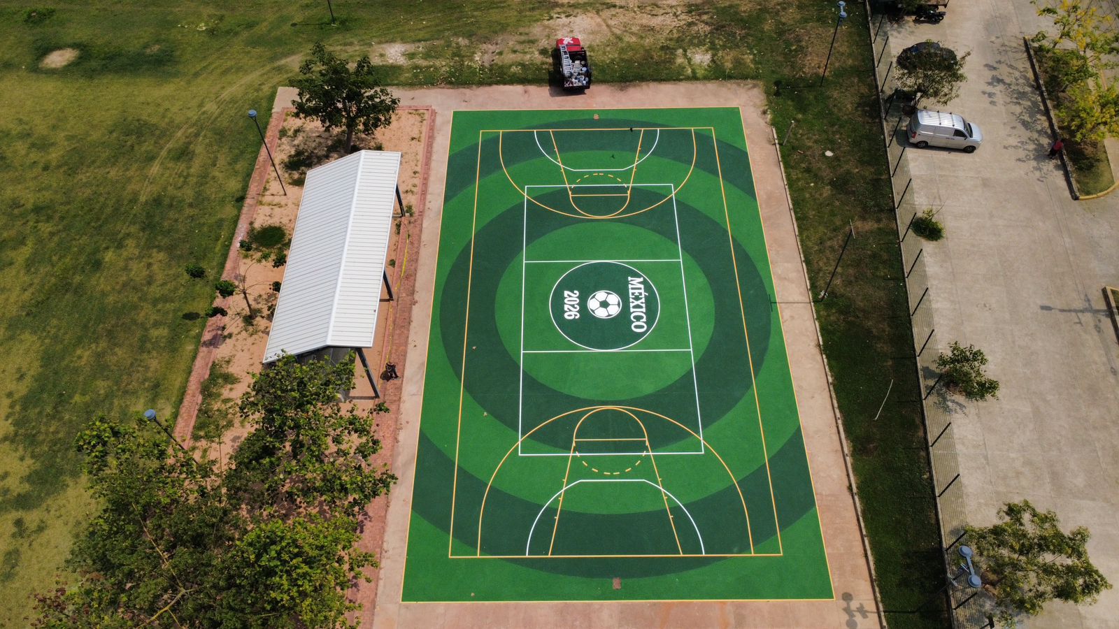 Cancha multifuncional verde con diseño de círculos concéntricos y sello México 2026 al centro pintada con sistema acrílico antiderrapante PLAYKO vista aérea perspectiva