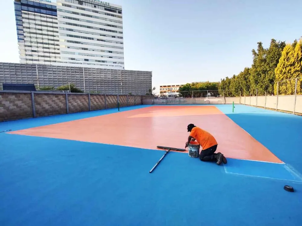 Cancha deportiva azul con zona interior naranja durante la aplicación del sistema acrílico PLAYKO